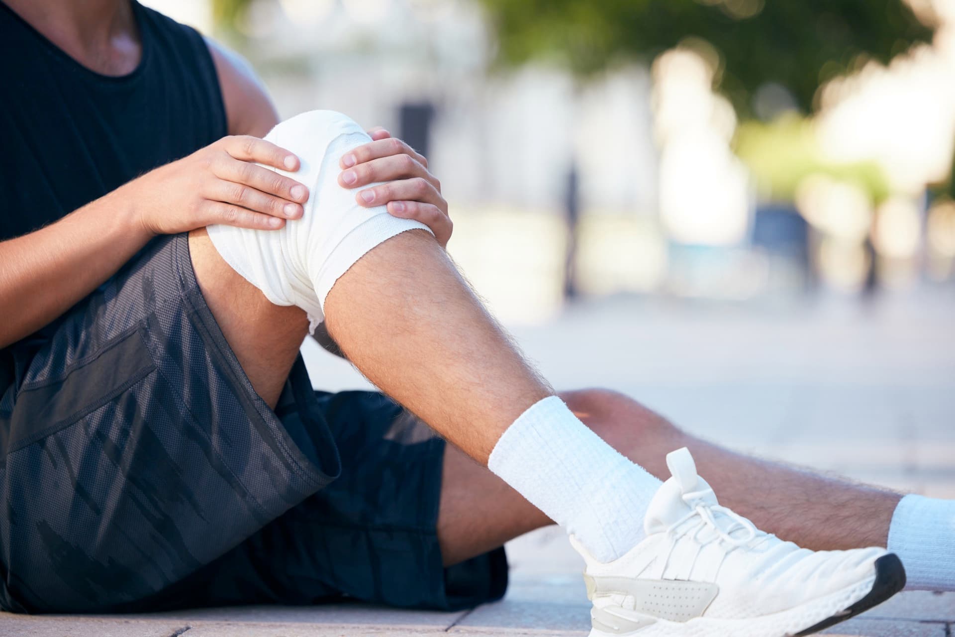 A runner outdoors clutching a bandaged knee after activity